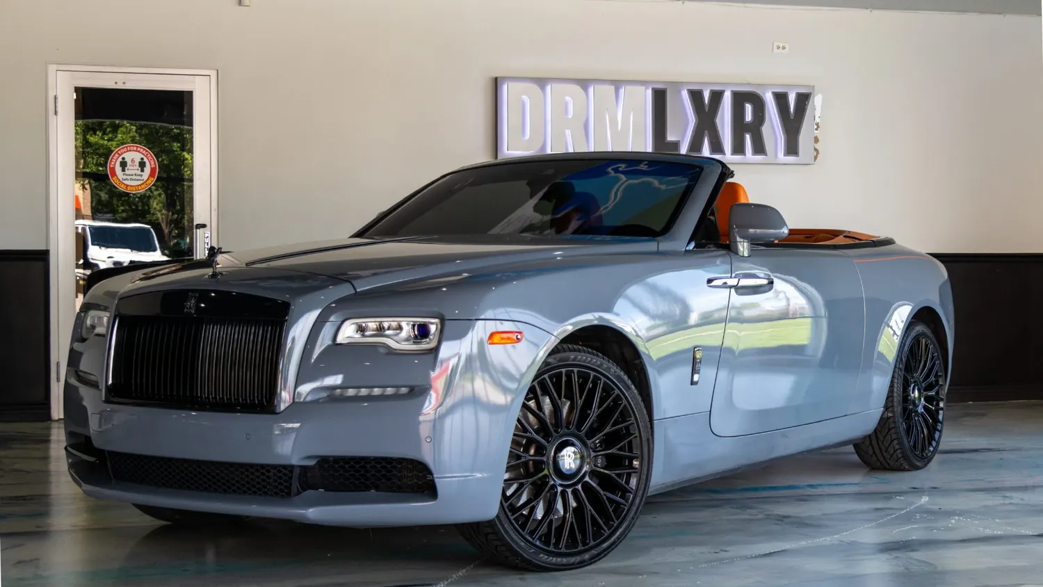 Silver Rolls-Royce Dawn rental in Detroit, front three-quarter view facing left, in the DRMLXRY showroom