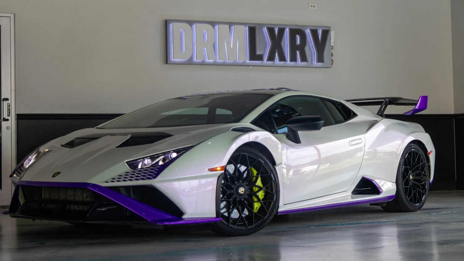 White Lamborghini Huracán STO rental in Detroit, front three-quarter view facing left, in the DRMLXRY showroom