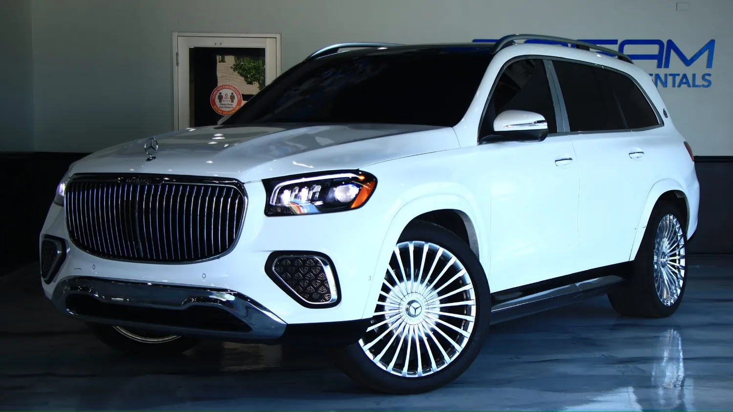 White 2024 Mercedes-Maybach GLS 600 rental in Detroit, front three-quarter view facing left, in the DRMLXRY showroom